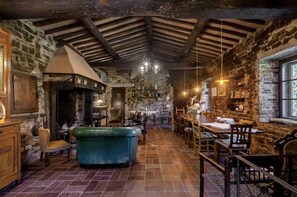 A rustic interior with stone walls, wooden beams, a fireplace, and a dining area with tables and chairs. - Apartment 'Rifugio sulla via di Volpaia' with Private Terrace, Wi-Fi and Air Conditioning (Radda in Chianti)