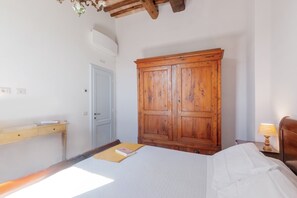 A bedroom with a wooden wardrobe, a bed with white bedding, a bedside table with a lamp, and a desk with a book. - Apartment 'Rifugio sulla via di Volpaia' with Private Terrace, Wi-Fi and Air Conditioning (Radda in Chianti)