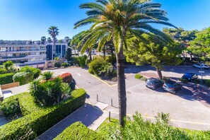 A parking area with cars, a palm tree, and a building with balconies in the background.