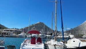 Un port de plaisance où sont amarrés de nombreux bateaux, un ciel bleu azur et, au loin, un grand navire de croisière.
