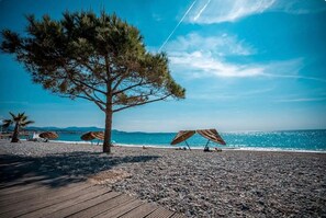 A beach with a wooden deck, umbrellas, and a tree.