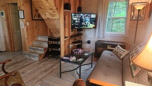 Ein gemütliches Blockhaus-Interieur mit einer Holztreppe, einem Fernseher, einer Couch und einem kleinen Tisch mit Büchern.