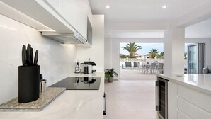 Une cuisine moderne dotée d’un plan de travail en marbre, d’un porte-ustensiles noir et offrant une vue sur l’espace extérieur aménagé en coin salon.