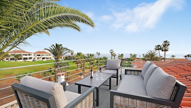 Un balcon avec mobilier d’extérieur, une vue sur un terrain de golf et des palmiers.