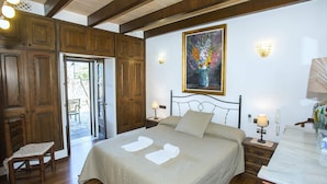A bedroom with a bed, two bedside tables, a chair, a painting, and a door leading to an outdoor area.