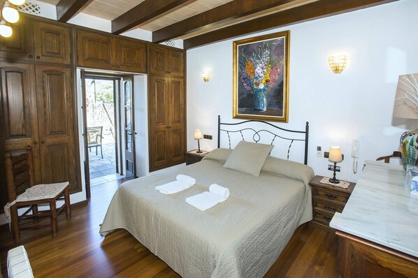 Une chambre à coucher comprenant un lit, deux tables de chevet, une chaise, un tableau et une porte donnant sur un espace extérieur.