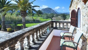 A balcony with a stone balustrade, two chairs, and a view of a green landscape with trees and mountains in the background.