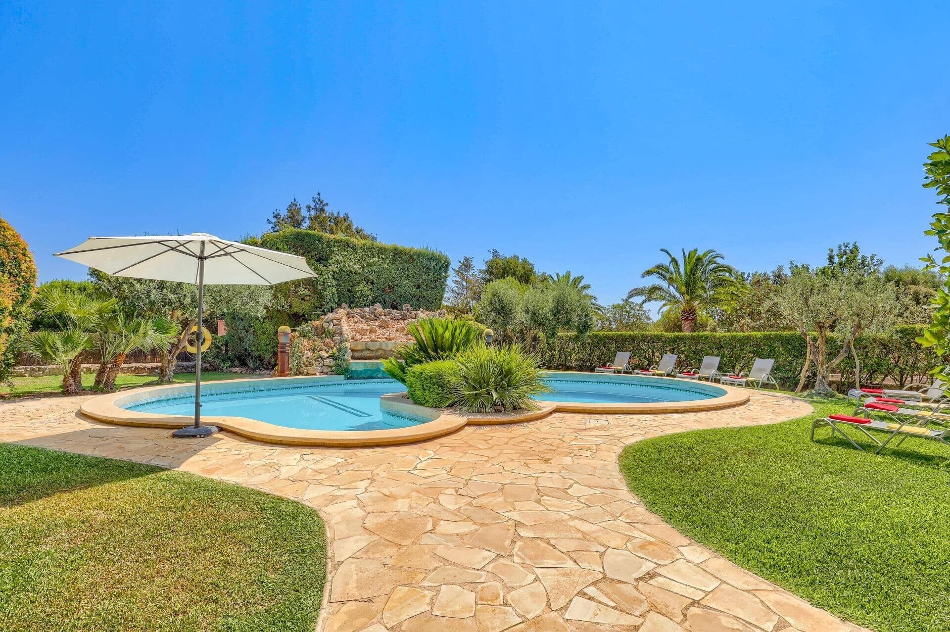 A landscaped outdoor area with a swimming pool, lounge chairs, and a stone pathway.