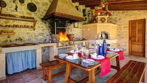 A rustic stone kitchen with a wood-fired oven, a stone wall, and a wooden ceiling. - Villa Busqueroles by Villa Plus (Pollença)