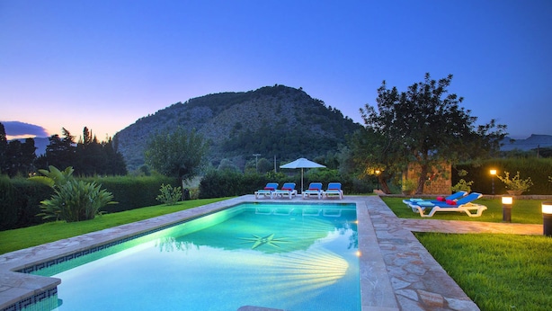 A swimming pool with lounge chairs and umbrellas, surrounded by a well-maintained lawn and a stone pathway. - Villa Busqueroles by Villa Plus (Pollença)