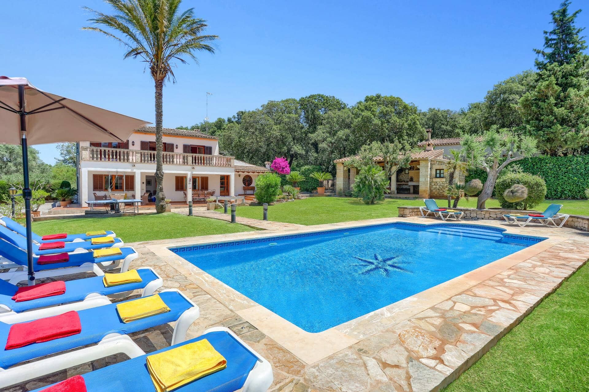 A swimming pool with lounge chairs and towels, surrounded by a well-maintained lawn and a house with a balcony.