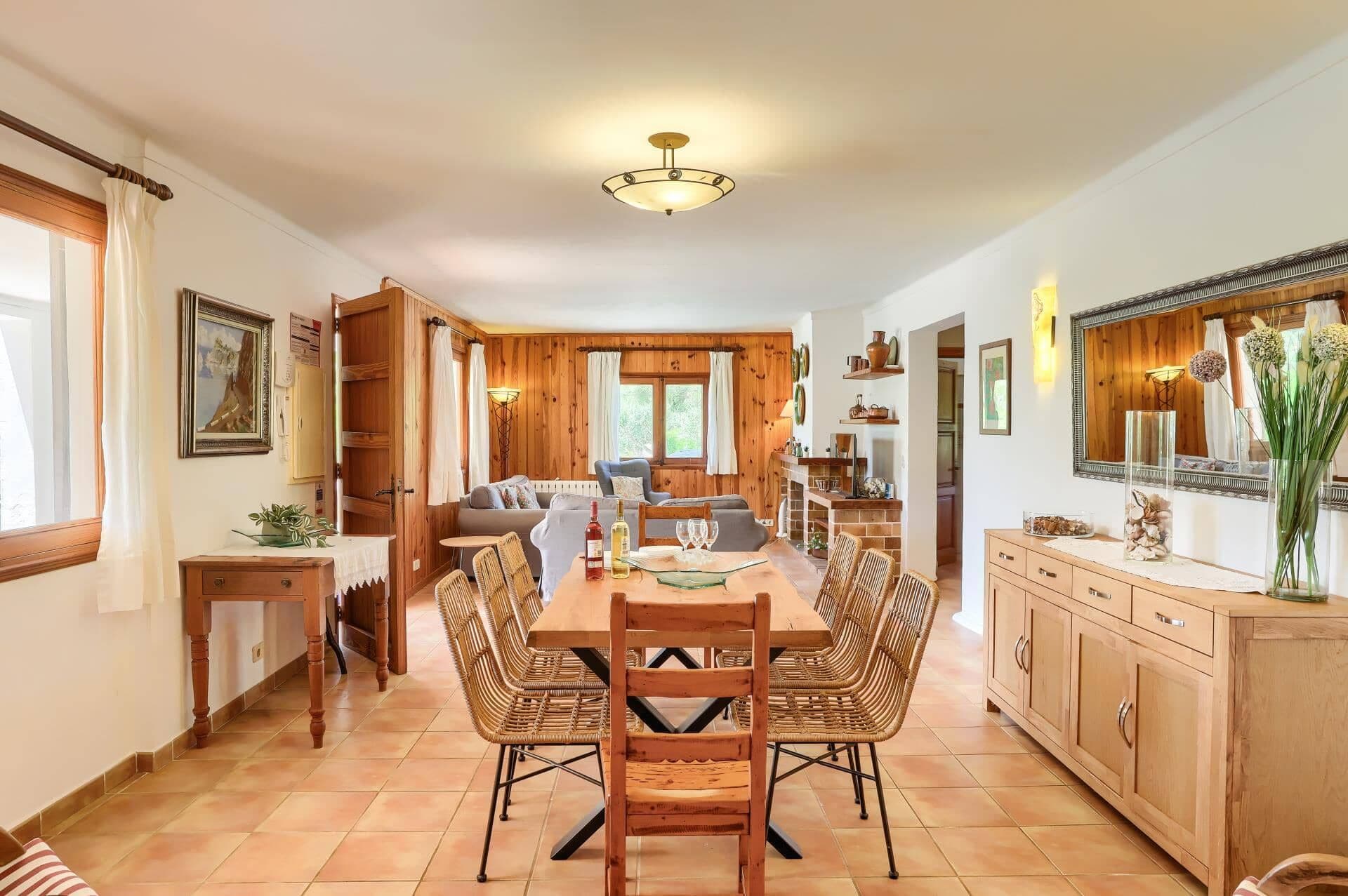 A dining area with a wooden table and chairs, a sofa, and a kitchen in the background.