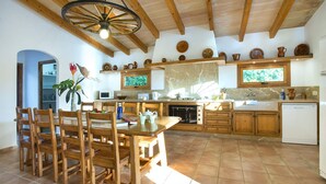 A rustic kitchen with wooden beams, a dining area with a wooden table and chairs, and a tiled floor. - Villa Busqueroles by Villa Plus (Pollença)