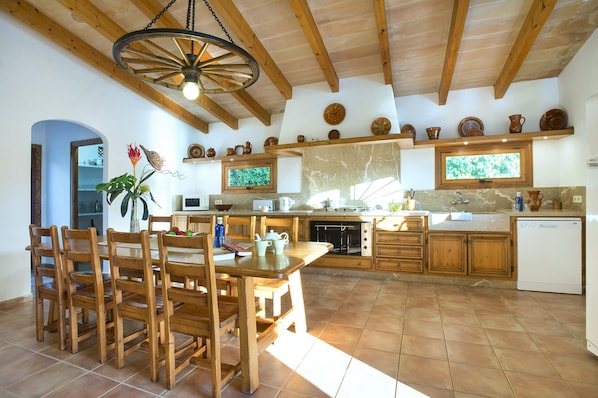 Una cocina rústica con vigas de madera, un comedor con mesa y sillas de madera, y piso de baldosas.