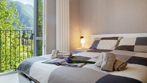 A hotel room with a large bed, a nightstand with a lamp, and a view of mountains through a balcony. - Apartment "Il Sole Di Calde Lago Maggiore 504" with Lake View, Balcony & Wi-Fi (castelveccana)