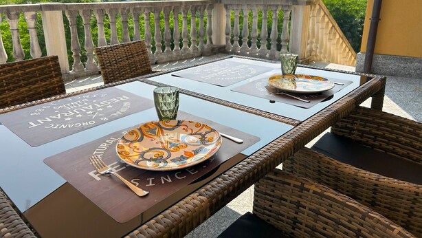 A dining table with placemats, a glass, and cutlery set on a balcony overlooking a mountainous landscape. - Apartment "Il Sole Di Calde Lago Maggiore 504" with Lake View, Balcony & Wi-Fi (castelveccana)
