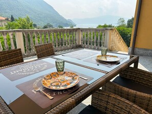 Un tavolo da pranzo con tovagliette, un bicchiere e posate su un balcone con vista su un paesaggio montuoso.