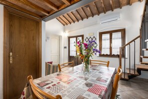 A dining area with a table set for four, wooden chairs, a vase with flowers, and a staircase to the right.