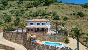 Ein zweistöckiges Haus mit Swimmingpool, umgeben von einer Steinmauer und Palmen.