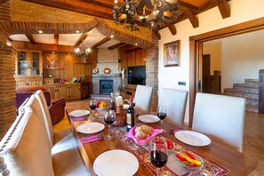 Un coin repas avec une longue table en bois dressée pour le repas, une cheminée et un téléviseur fixé au mur.
