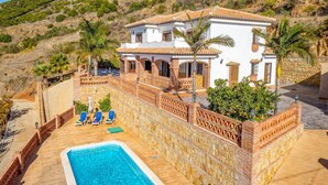Ein zweistöckiges Haus mit Pool, einer Terrasse mit Liegestühlen und einer Steinmauer.