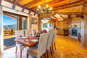 A dining area with a table set for four, a fireplace, and a kitchen in the background. - Villa Biznaga by Villa Plus (Valtocado)