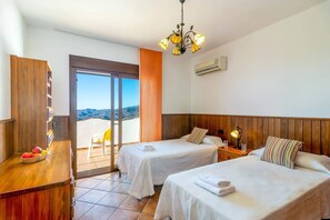 A hotel room with two beds, a wooden desk, a fruit basket, a balcony with a view, and a chandelier. - Villa Biznaga by Villa Plus (Valtocado)