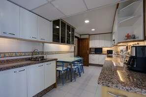 Una cocina con armarios blancos, encimera de granito, una mesa de comedor con sillas azules y un horno empotrado.