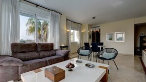 A modern living room with a sofa, a coffee table, and a dining area with chairs. - Apartment Costalita with Sea View, Terrace, Shared Pool & Wi-Fi (Estepona)