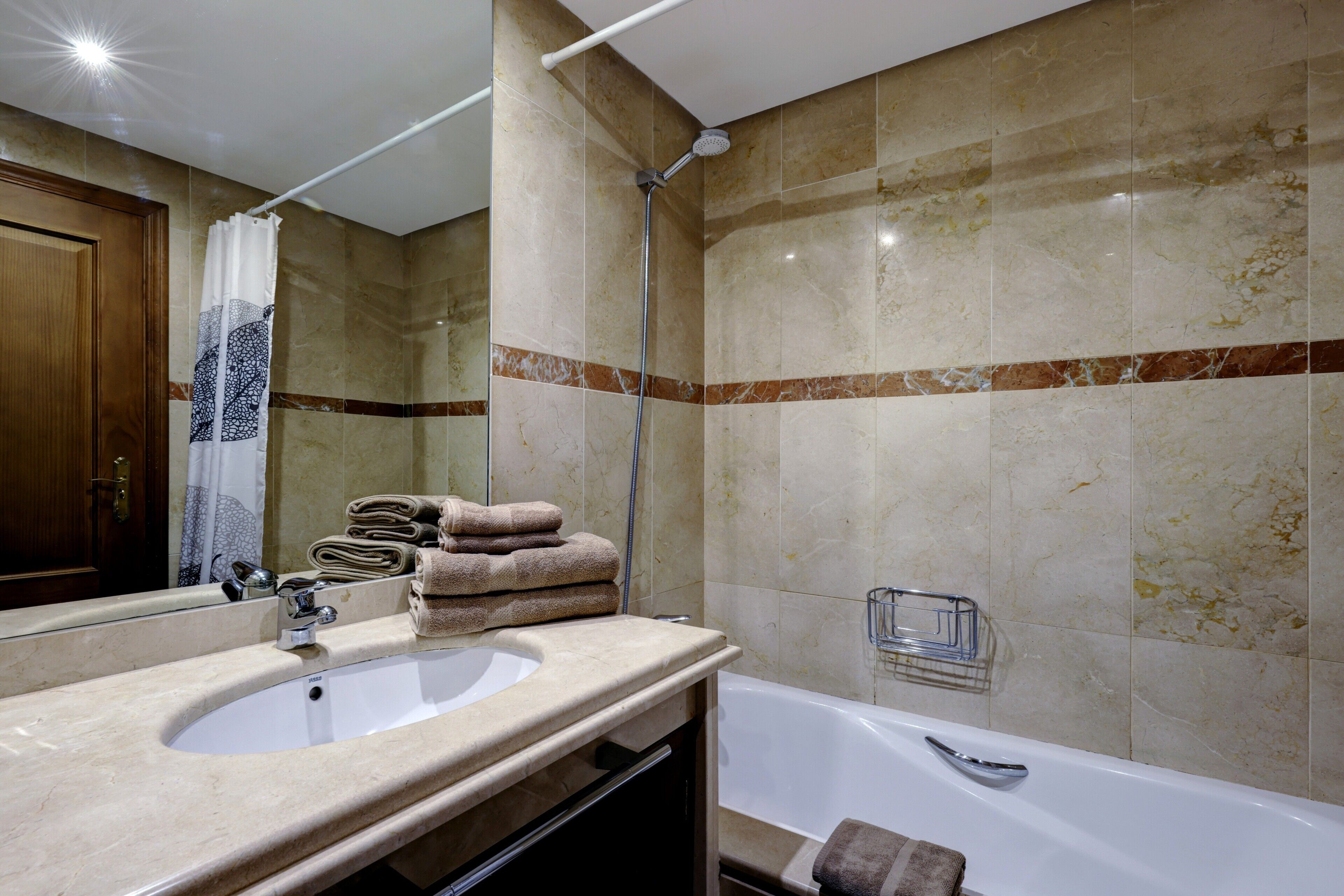 A bathroom with a sink, mirror, shower, and towel rack.