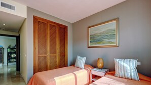 A bedroom with two beds, a wooden wardrobe, a painting, and a nightstand with a lamp. - Apartment Costalita with Sea View, Terrace, Shared Pool & Wi-Fi (Estepona)