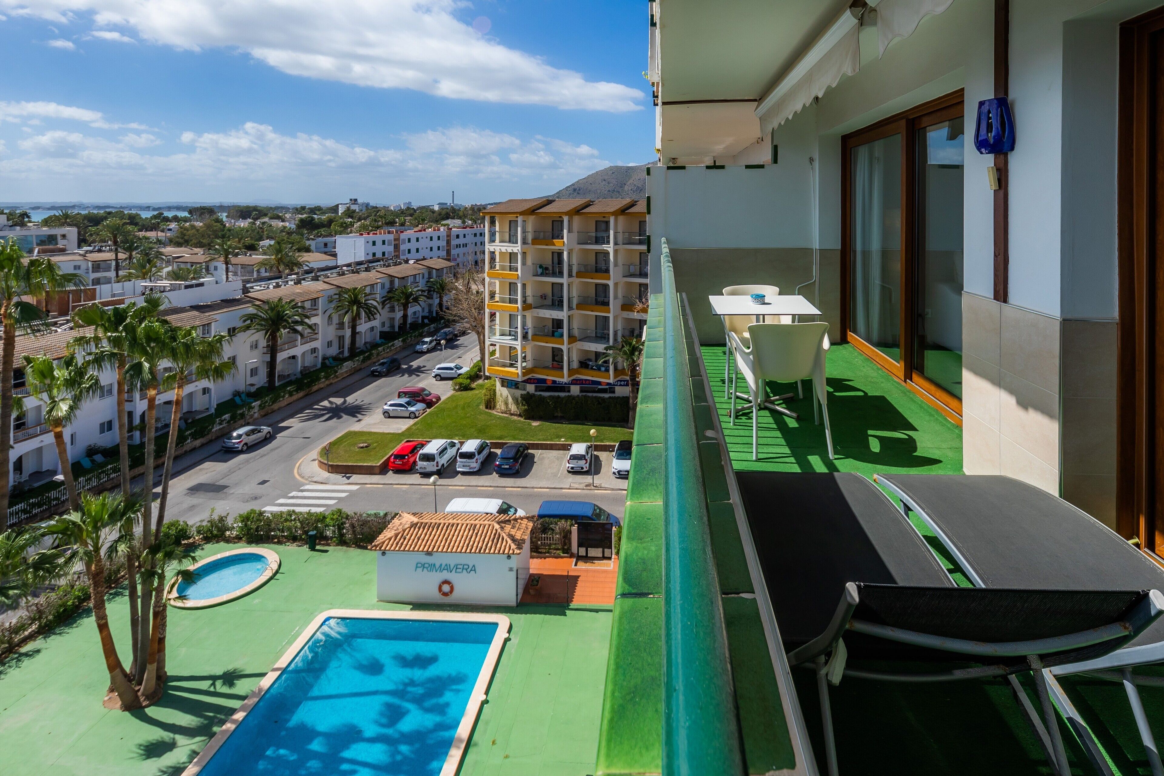 En balkong med utsikt över en swimmingpool, en parkeringsplats och en byggnad med flera våningar.