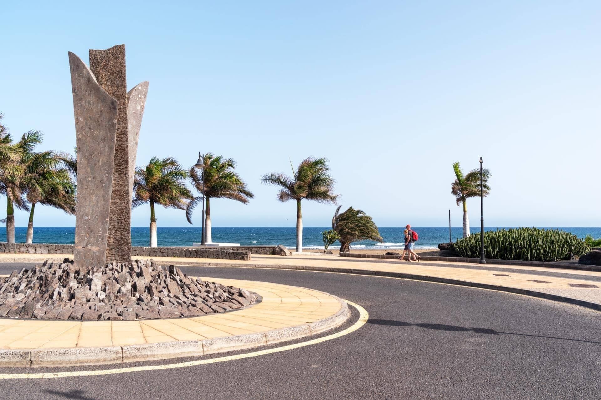 Un rond-point agrémenté de palmiers, orné d’une sculpture centrale et offrant une vue sur la mer.
