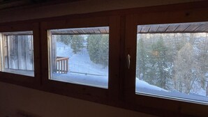 Tres ventanas con marcos de madera, cada una mostrando una vista nevada del exterior con árboles y una terraza de madera.