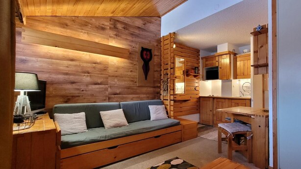 Un interior de cabaña acogedor, con un sofá de madera, una pequeña mesa de comedor y una kitchenette.