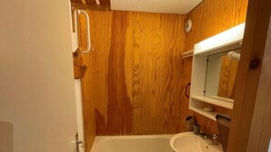 Un baño pequeño con pared de madera, una bañera blanca, un lavamanos y un inodoro.