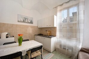 A compact kitchen with a dining table, chairs, a vase of flowers, and a window with a curtain.