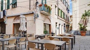 An outdoor café with tables and chairs, a building with a sign reading 'Ristorante Piazza,' and a potted plant.