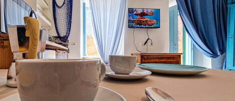 A kitchen with a dining table set for two, a hanging hammock, and a TV mounted on the wall.