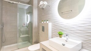 Un bagno moderno con doccia vetrata, uno specchio rotondo e un lavabo con una pianta in vaso.