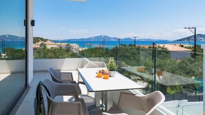 Un balcone con tavolo e sedie, affaccia su un paesaggio costiero con case e montagne.
