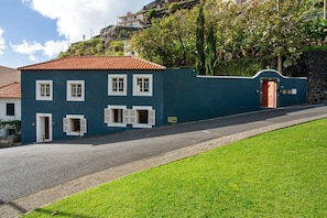 A two-story building with a red-tiled roof, a blue exterior, and a paved driveway. - Holiday Home 'Calheta Beach House T1' with Mountain View, Private Terrace and Wi-Fi (Lombo Do Doutor)