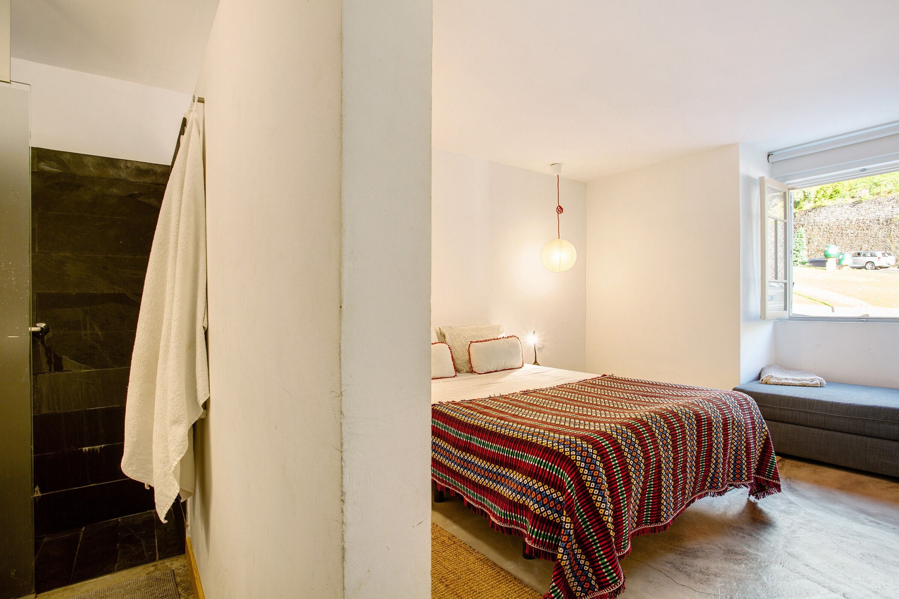 A bedroom with a bed, a window with a view, and a bathroom with a shower.