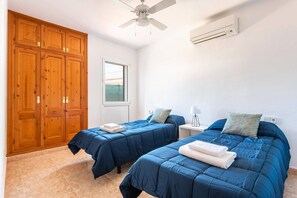 A bedroom with two beds, a ceiling fan, an air conditioning unit, wooden wardrobes, and a window.