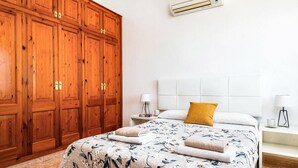 A bedroom with a large wooden wardrobe, a bed with floral bedding, and a white headboard. - Villa Bini Mestral by Villa Plus (Binibeca)