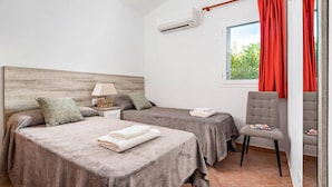 Hotelkamer met twee bedden, een stoel, een raam met rode gordijnen, een airconditioning en een lamp op een nachtkastje.