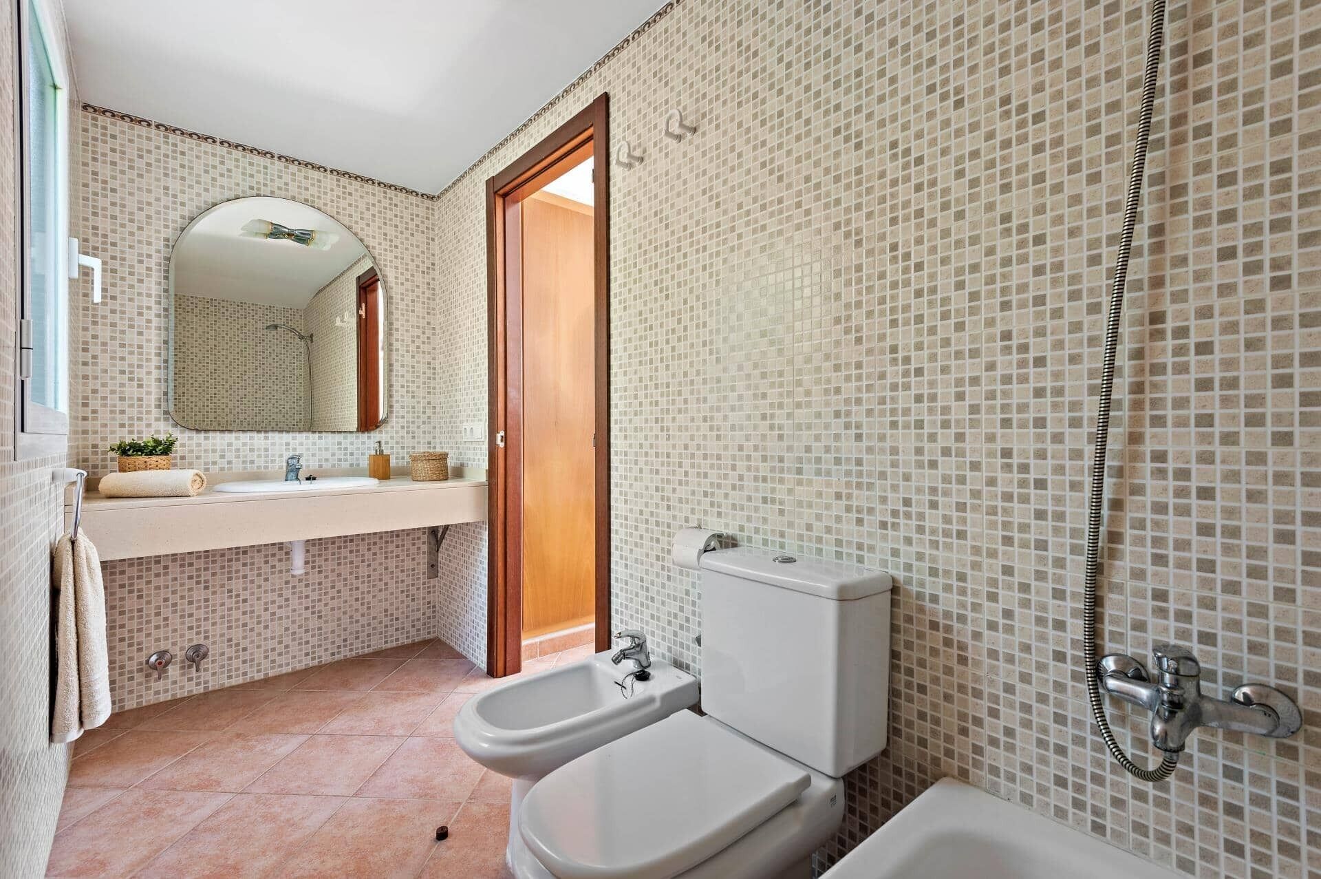 A bathroom with a tiled floor, a sink with a mirror, two toilets, and a shower.