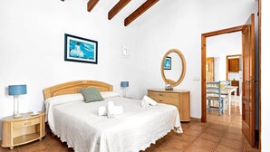 A bedroom with a bed, bedside tables, a mirror, and a view into the kitchen. - Villa Bini Anna by Villa Plus (Binibeca)