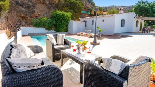 Un patio con mobili in vimini, una piscina e vista su un pendio roccioso.