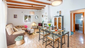 Un'ampia zona giorno con divano, tavolo da pranzo e sedie, travi in legno al soffitto e vista sulla città dalla finestra.